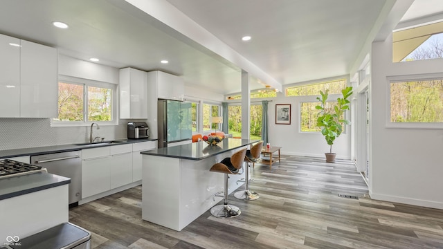 kitchen featuring dark countertops, white cabinetry, a sink, backsplash, and stainless steel appliances