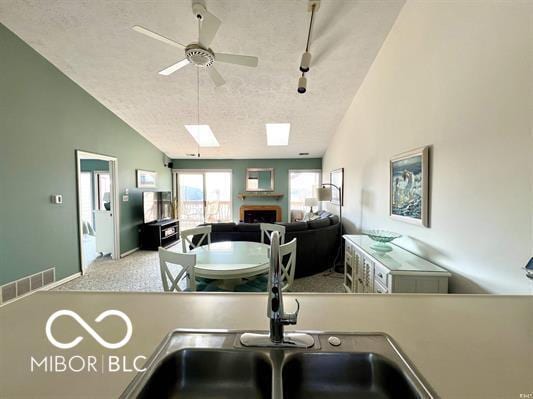 kitchen featuring vaulted ceiling with skylight, a ceiling fan, a textured ceiling, visible vents, and a sink