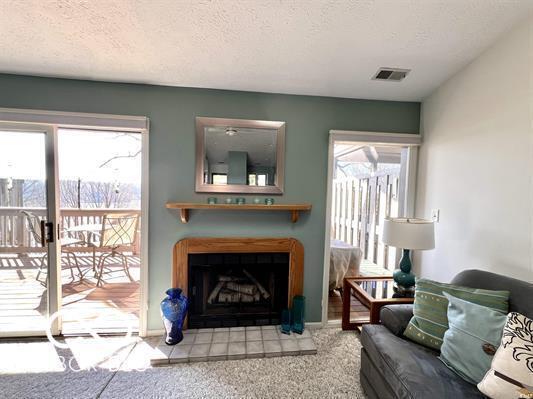 carpeted living area featuring a textured ceiling, visible vents, and a tile fireplace