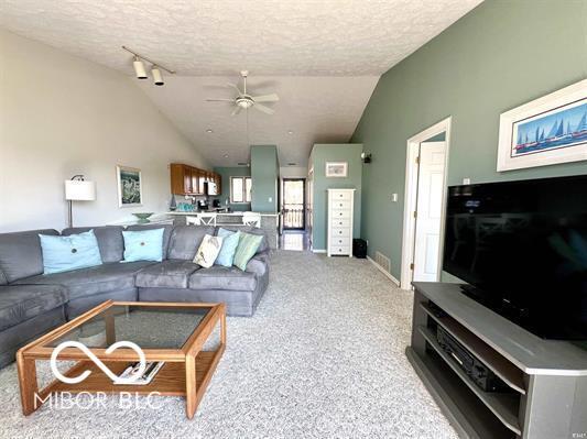 living room with a textured ceiling, light colored carpet, ceiling fan, and lofted ceiling