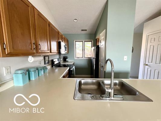 kitchen featuring visible vents, brown cabinets, a sink, light countertops, and stainless steel appliances