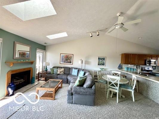 carpeted living room featuring a fireplace, a ceiling fan, lofted ceiling with skylight, and a textured ceiling