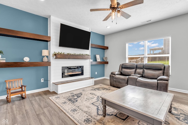 living room with visible vents, wood finished floors, baseboards, a large fireplace, and a ceiling fan