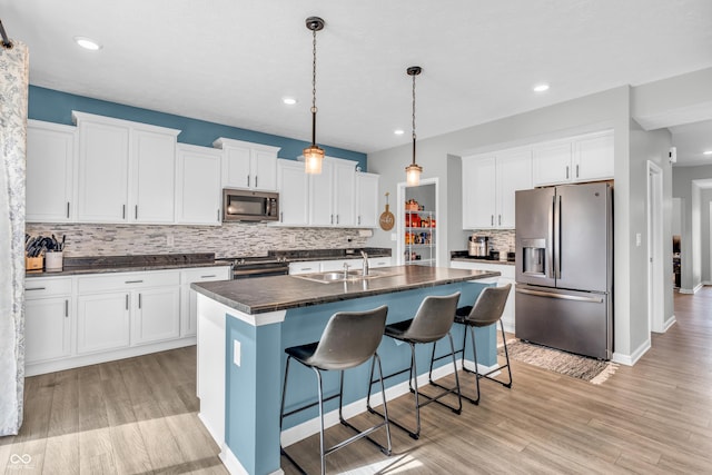 kitchen featuring backsplash, dark countertops, appliances with stainless steel finishes, a sink, and an island with sink