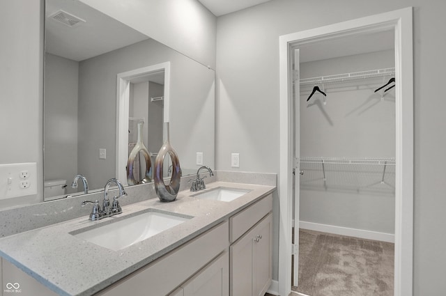 full bath featuring a sink, a walk in closet, double vanity, and visible vents