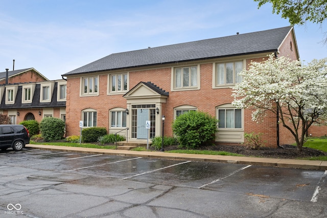 view of front of home featuring brick siding, a shingled roof, and uncovered parking