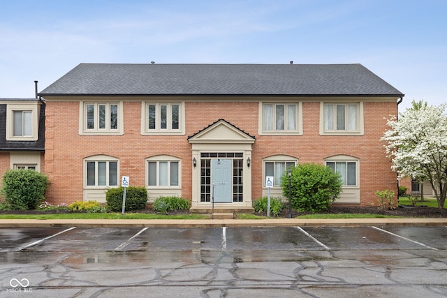 view of front of property with brick siding, uncovered parking, and roof with shingles