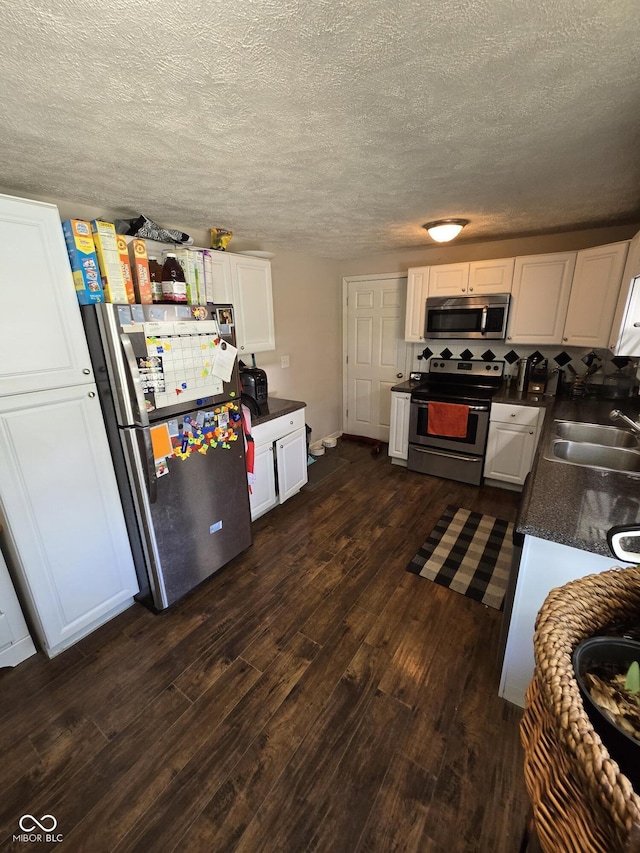 kitchen with dark countertops, appliances with stainless steel finishes, a sink, dark wood finished floors, and white cabinetry