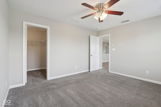 unfurnished bedroom with carpet flooring, a spacious closet, baseboards, and a ceiling fan