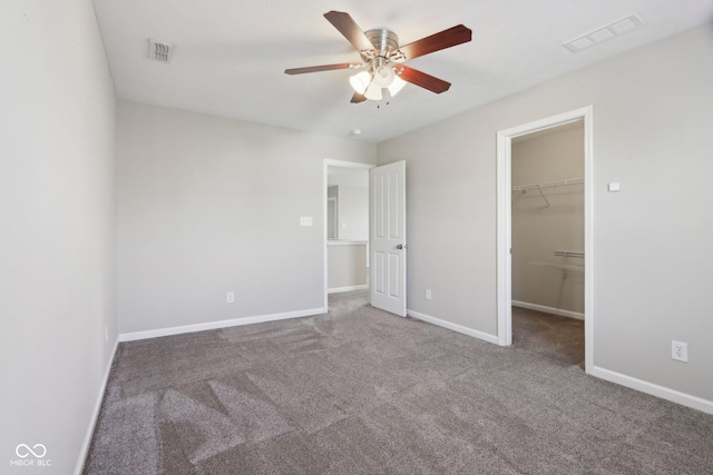 unfurnished bedroom with carpet floors, a walk in closet, baseboards, and a ceiling fan