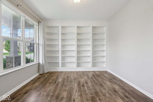 empty room with dark wood-type flooring, baseboards, and built in shelves