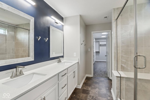 bathroom featuring a shower stall, baseboards, a walk in closet, double vanity, and stone finish floors