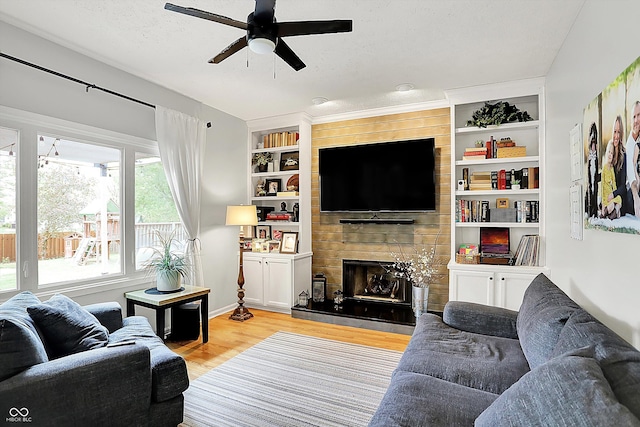 living area featuring ceiling fan, built in features, a large fireplace, wood finished floors, and baseboards