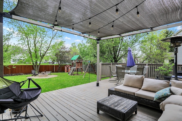 wooden terrace featuring a fenced backyard, a playground, an outdoor living space with a fire pit, a yard, and outdoor dining space