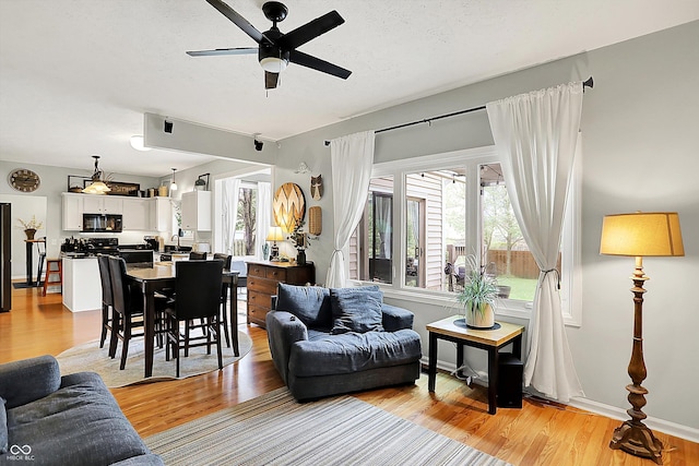 living area featuring baseboards, ceiling fan, and light wood-style flooring