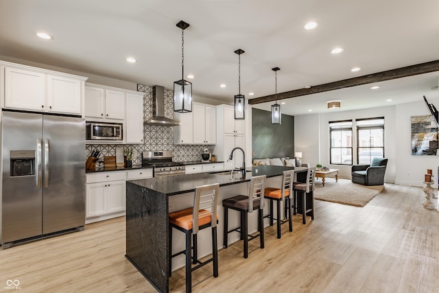 1534 Fletcher Ave, Indianapolis, IN 46203 - kitchen featuring stainless steel appliances, wall chimney exhaust hood, dark countertops, light wood-style floors, and an island with sink