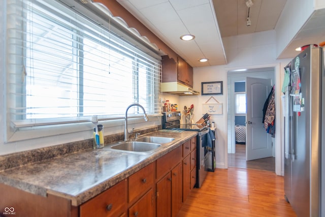 kitchen featuring brown cabinets, appliances with stainless steel finishes, a sink, wall chimney exhaust hood, and light wood-type flooring