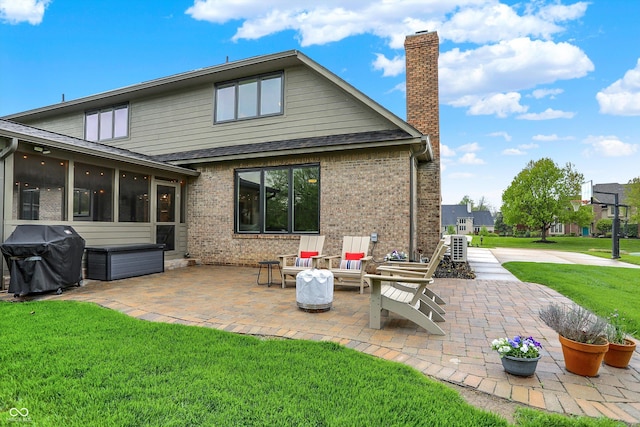 back of house with a chimney, a sunroom, a shingled roof, a patio area, and a lawn