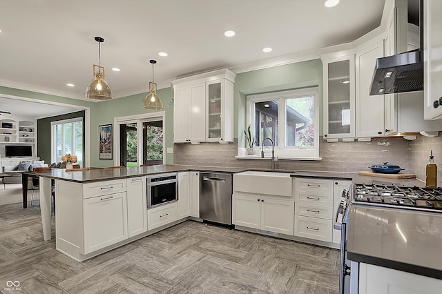 kitchen featuring appliances with stainless steel finishes, dark countertops, a sink, a peninsula, and white cabinetry