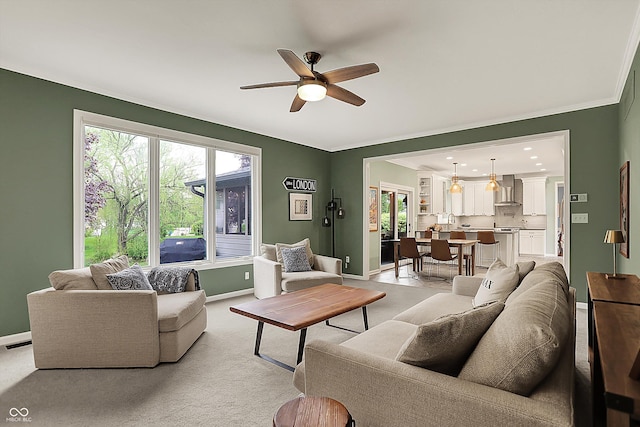 living room featuring light colored carpet, a ceiling fan, baseboards, visible vents, and ornamental molding
