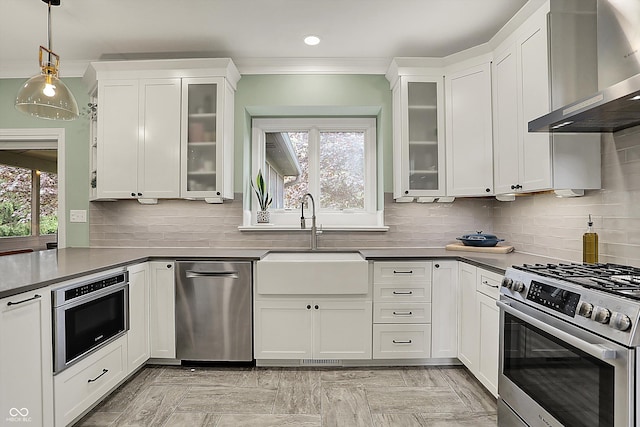 kitchen featuring ornamental molding, wall chimney exhaust hood, white cabinets, a sink, and appliances with stainless steel finishes