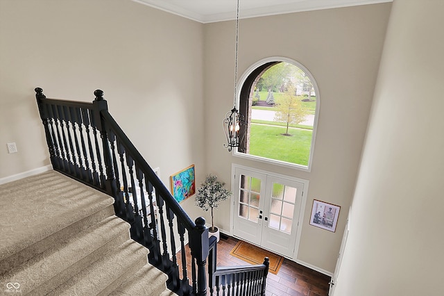 staircase featuring crown molding, an inviting chandelier, french doors, baseboards, and wood finished floors