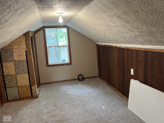additional living space with wood walls, baseboards, light colored carpet, a textured ceiling, and vaulted ceiling