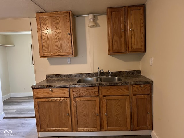 kitchen featuring baseboards, dark countertops, brown cabinetry, and a sink