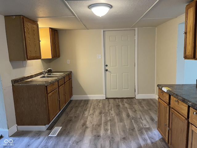 kitchen featuring visible vents, dark countertops, baseboards, a sink, and dark wood finished floors