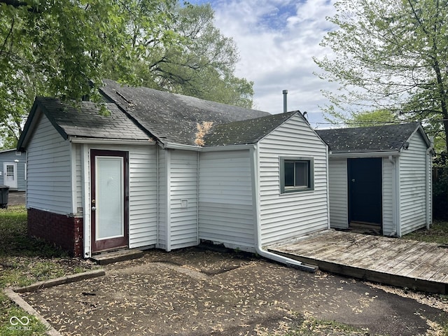 rear view of property featuring roof with shingles, a storage unit, and an outbuilding