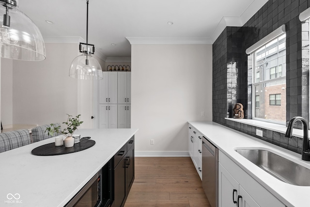kitchen with crown molding, wood finished floors, dishwasher, a sink, and light countertops