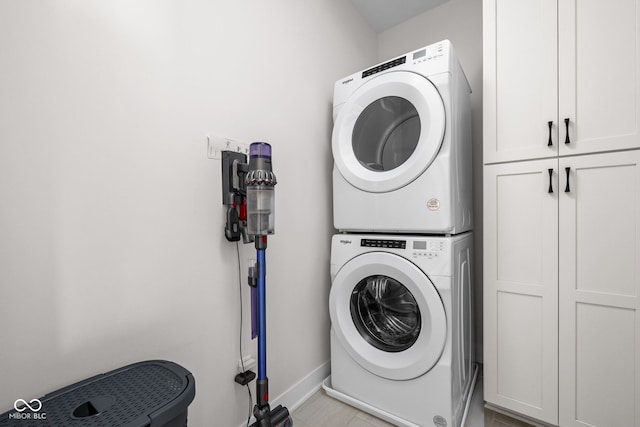 laundry room with baseboards, cabinet space, and stacked washer / drying machine