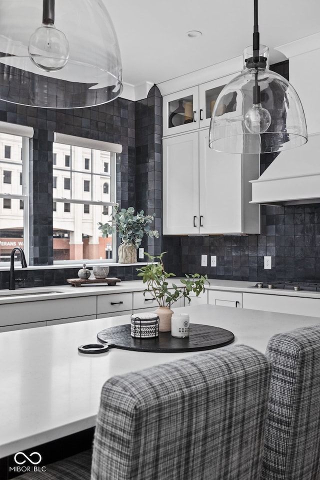kitchen with a sink, cooktop, white cabinetry, tasteful backsplash, and glass insert cabinets
