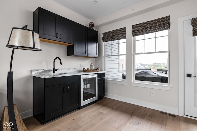 kitchen featuring wine cooler, dark cabinets, a sink, and visible vents