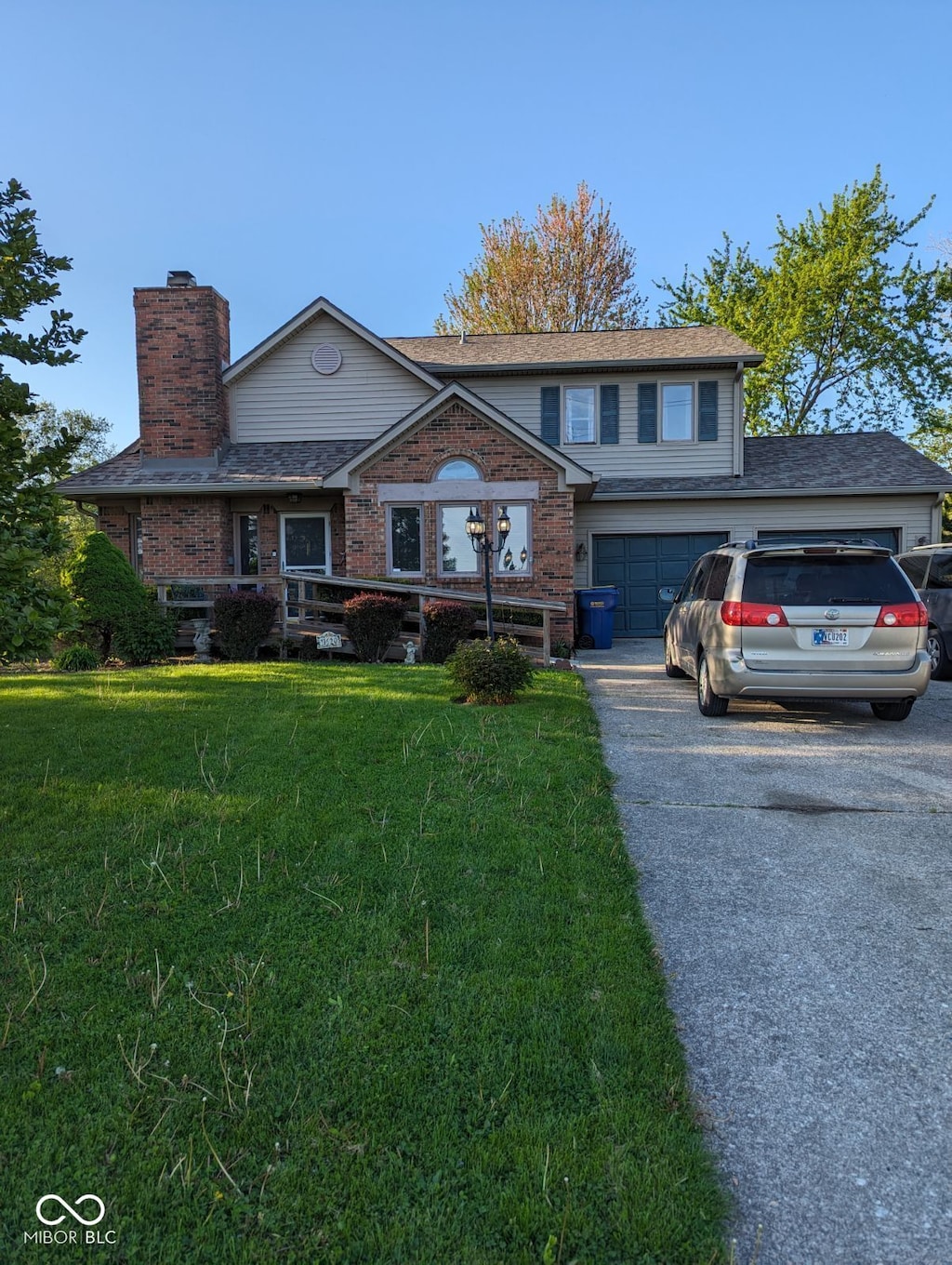 view of front facade featuring driveway, a chimney, a front lawn, brick siding, and a shingled roof