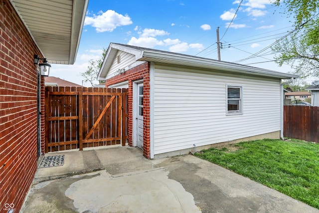 view of property exterior with fence, brick siding, a gate, a patio, and a yard