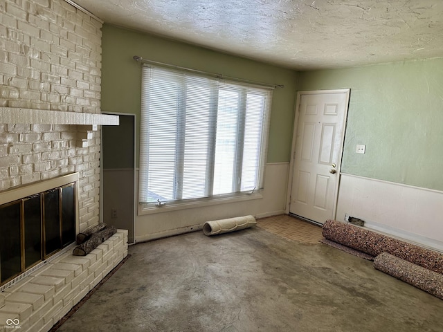 318 Elva St, Anderson, IN 46013 - unfurnished living room featuring a brick fireplace, a textured ceiling, wainscoting, and a healthy amount of sunlight