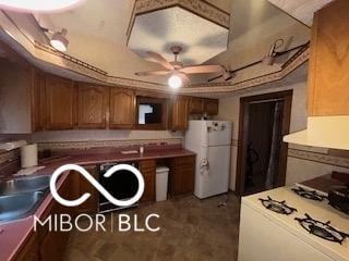 kitchen with white appliances, a ceiling fan, a tray ceiling, and brown cabinetry