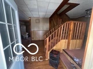 stairs with a drop ceiling, wood walls, and wood finished floors