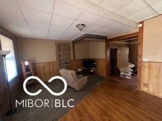 living room with wood finished floors, wood walls, a paneled ceiling, and a wainscoted wall