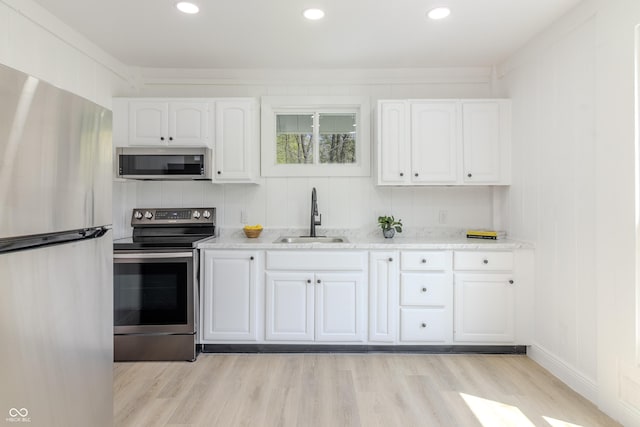 kitchen with stainless steel appliances, white cabinetry, a sink, and light wood-style flooring