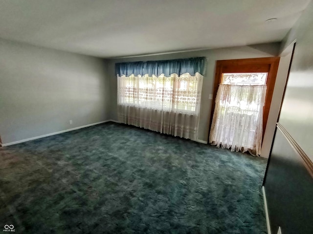 spare room with baseboards, plenty of natural light, and dark carpet