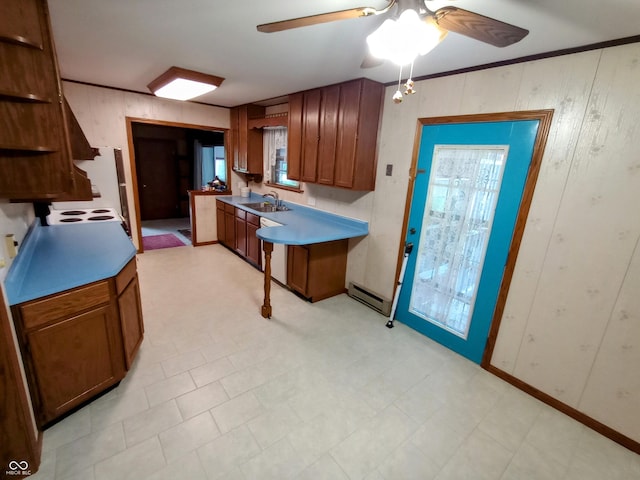 kitchen with a sink, brown cabinetry, a baseboard heating unit, light floors, and a ceiling fan
