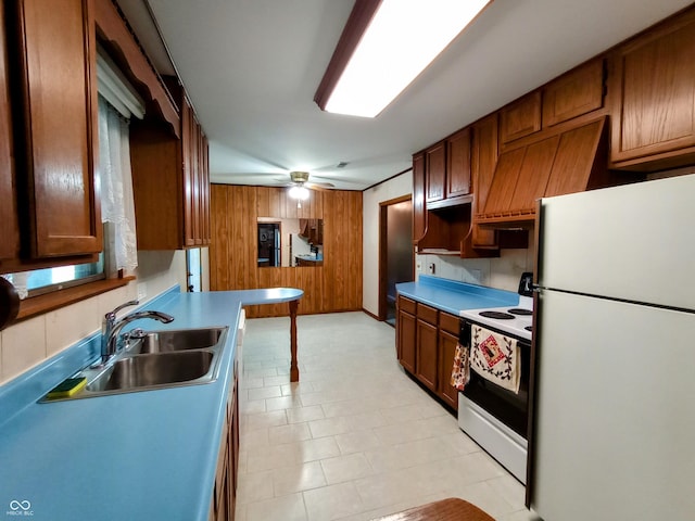 kitchen with a sink, wood walls, white appliances, light countertops, and a ceiling fan