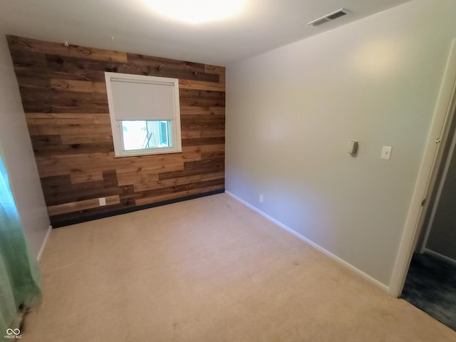 carpeted spare room with wood walls, baseboards, and visible vents
