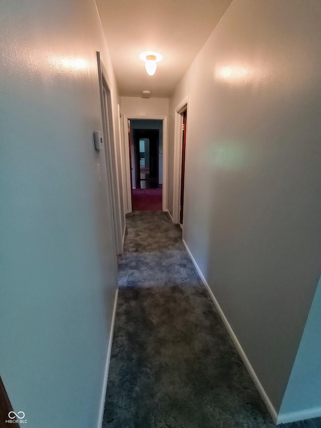 hall featuring baseboards and dark carpet