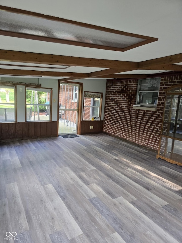 interior space featuring beam ceiling, wood finished floors, wainscoting, wooden walls, and brick wall