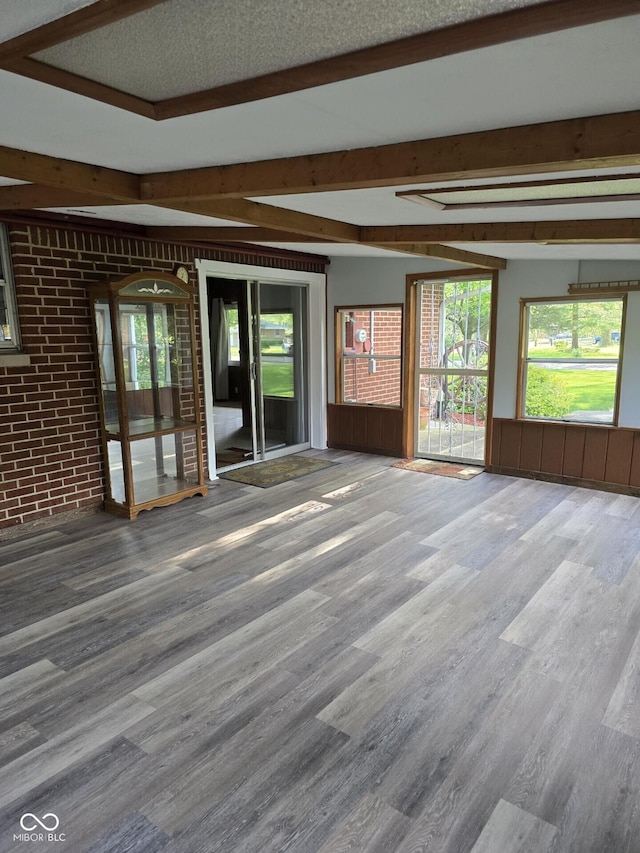 unfurnished room with a wealth of natural light, wood finished floors, beamed ceiling, and brick wall