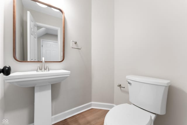 half bath featuring wood finished floors, toilet, and baseboards