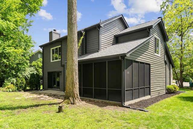 rear view of property featuring a chimney, a sunroom, a lawn, and roof with shingles